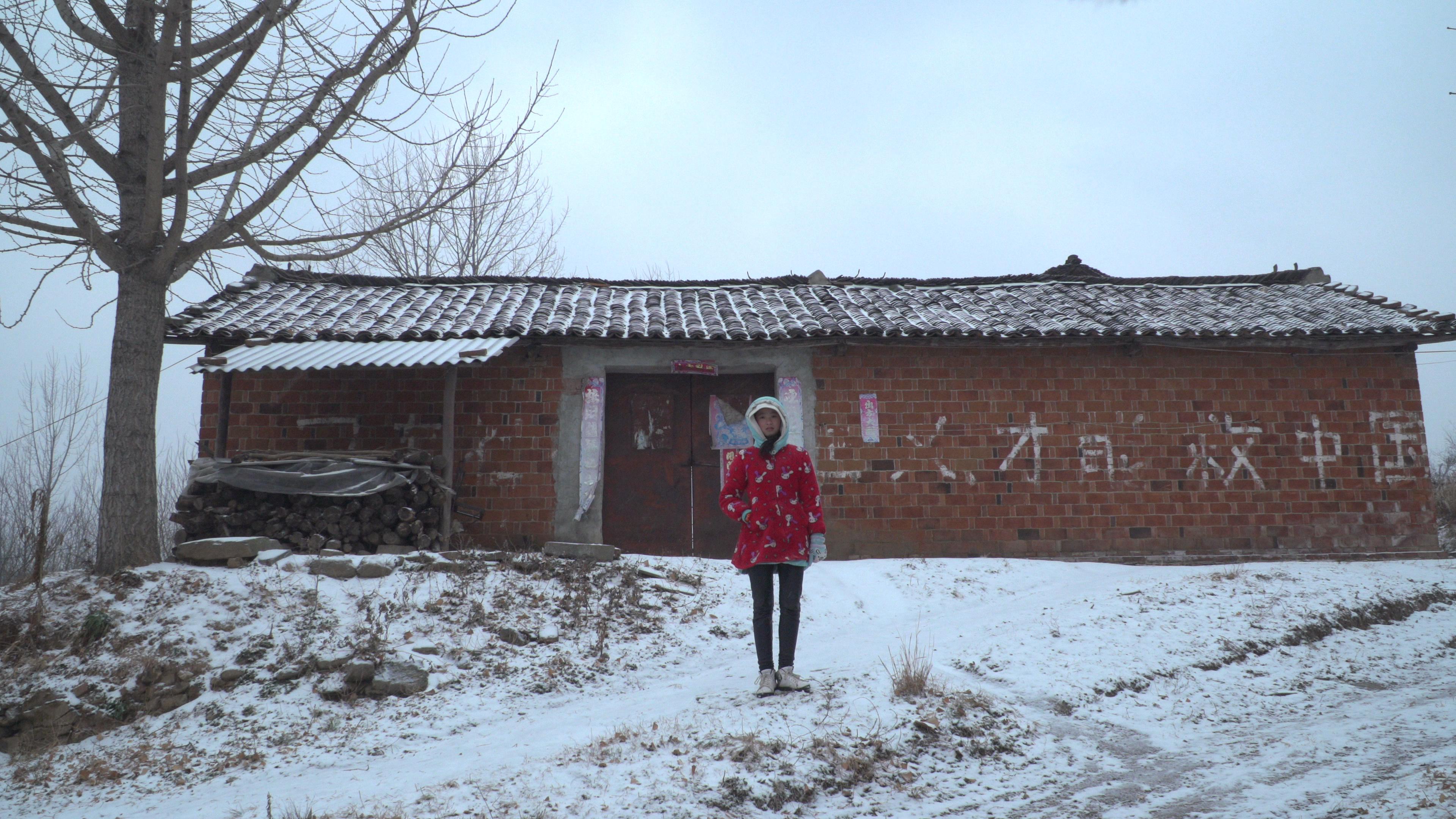 a figure stands in front a humble structure on snowy ground
