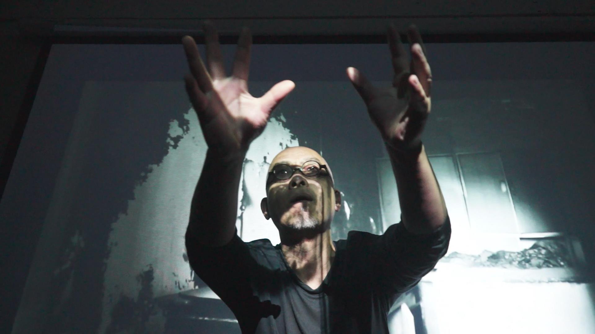 a man reaches out with both hands as projected images play in the background