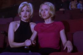 two blonde women clutch each other in a blue light