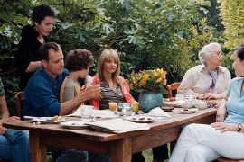 a multigenerational french family interacts around a garden-set dinner table
