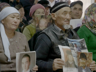 A still from the film All Static and Noise. Two individuals stand side by side holding up images of loved ones.