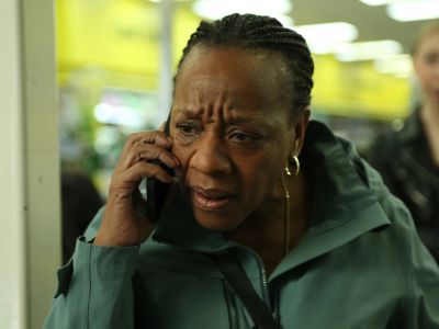 A black woman in a green jacket takes a phone call in a still from Hard Truths