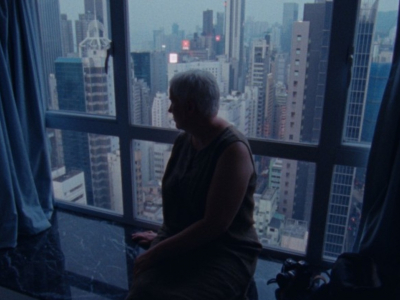 Anke Bak silhouetted in front of a window revealing the Hong Kong skyline, in a scene from WOOD AND WATER.